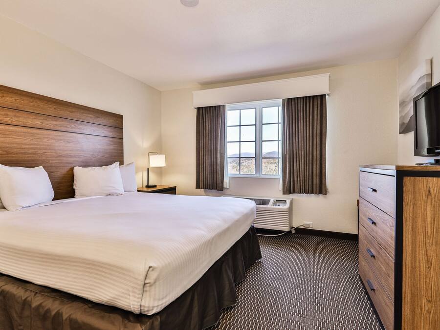A hotel room with a large bed, a desk, a television, and a window with curtains.