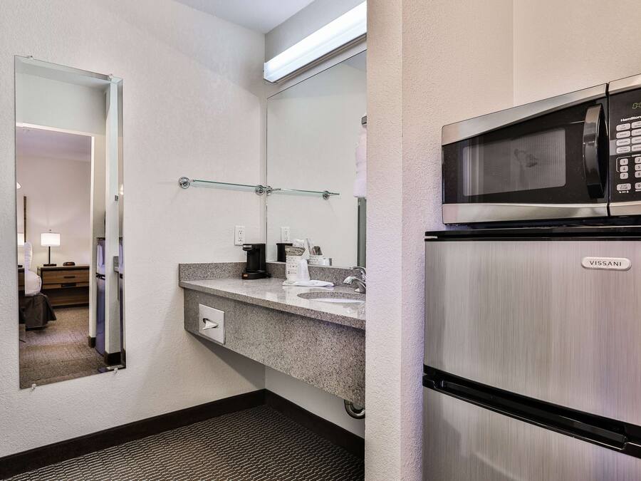Un baño de hotel con lavamanos, espejo y un refrigerador VISSANI.