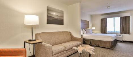 A hotel room with a sofa, a bed, a lamp, and a painting on the wall.