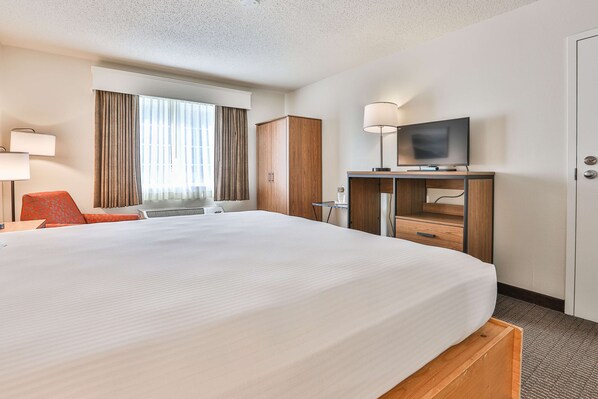 A hotel room with a large bed, a desk with a flat-screen TV, a wardrobe, and a window with curtains.