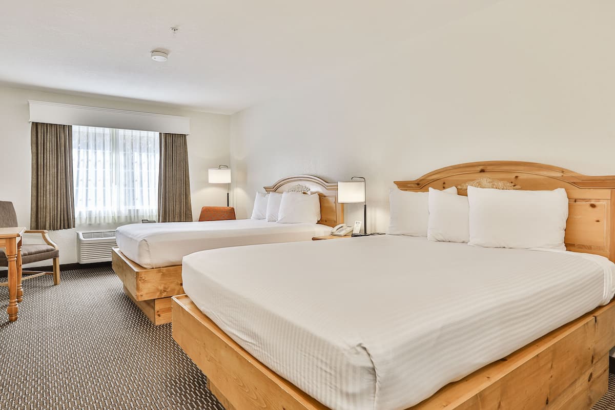 A hotel room with two beds, a desk, and a chair.