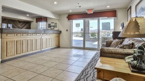 A reception area with a wooden counter, a couch, a lamp, and a view through the glass doors. - Best Western Mountain View Inn (Ellijay)