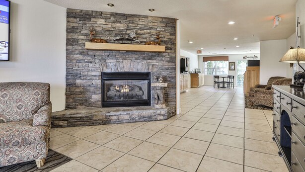 A spacious living room with a stone fireplace, a sofa, and a TV mounted on the wall. - Best Western Mountain View Inn (Ellijay)