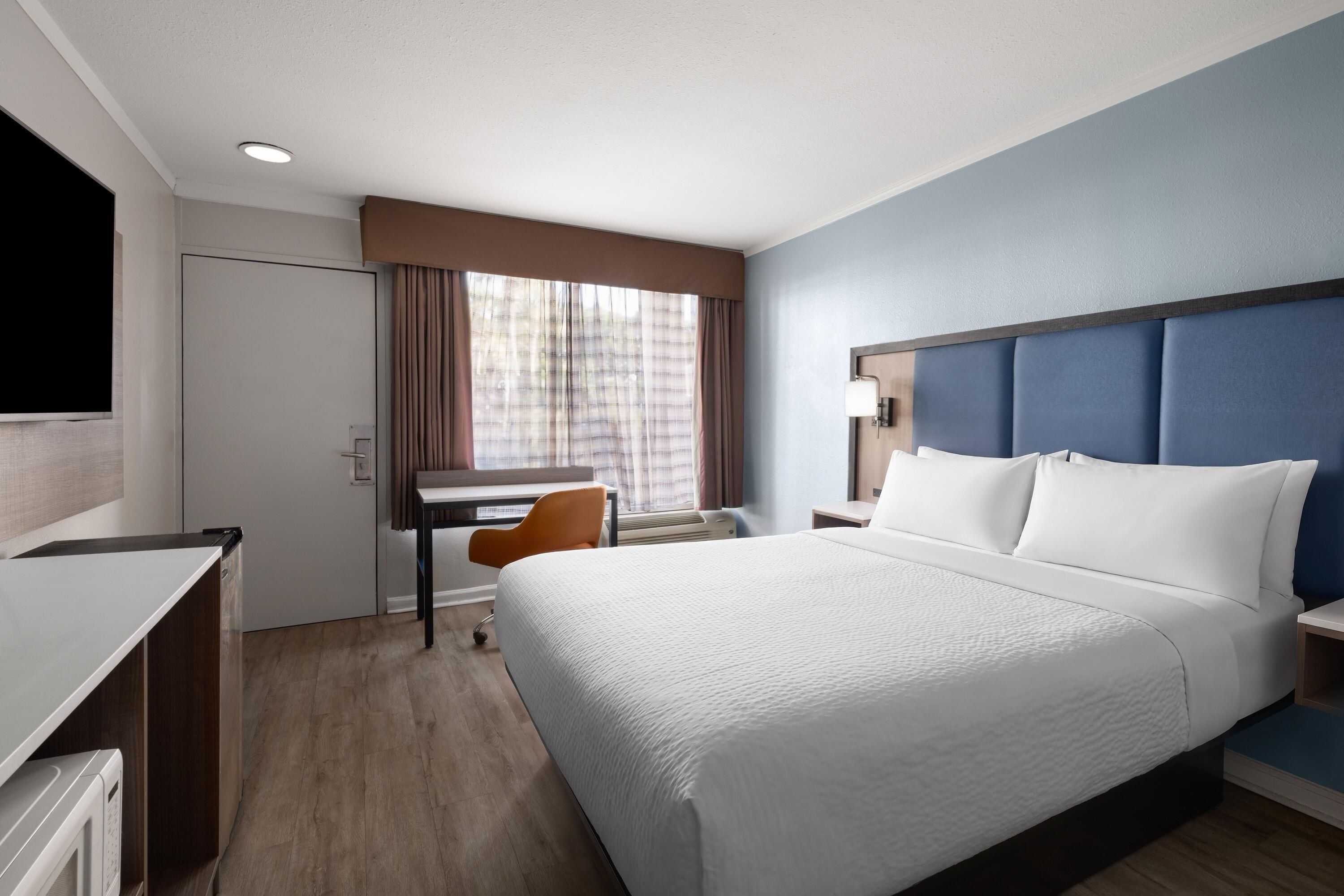 A hotel room with a bed, a desk, a chair, a television, and a window with curtains.