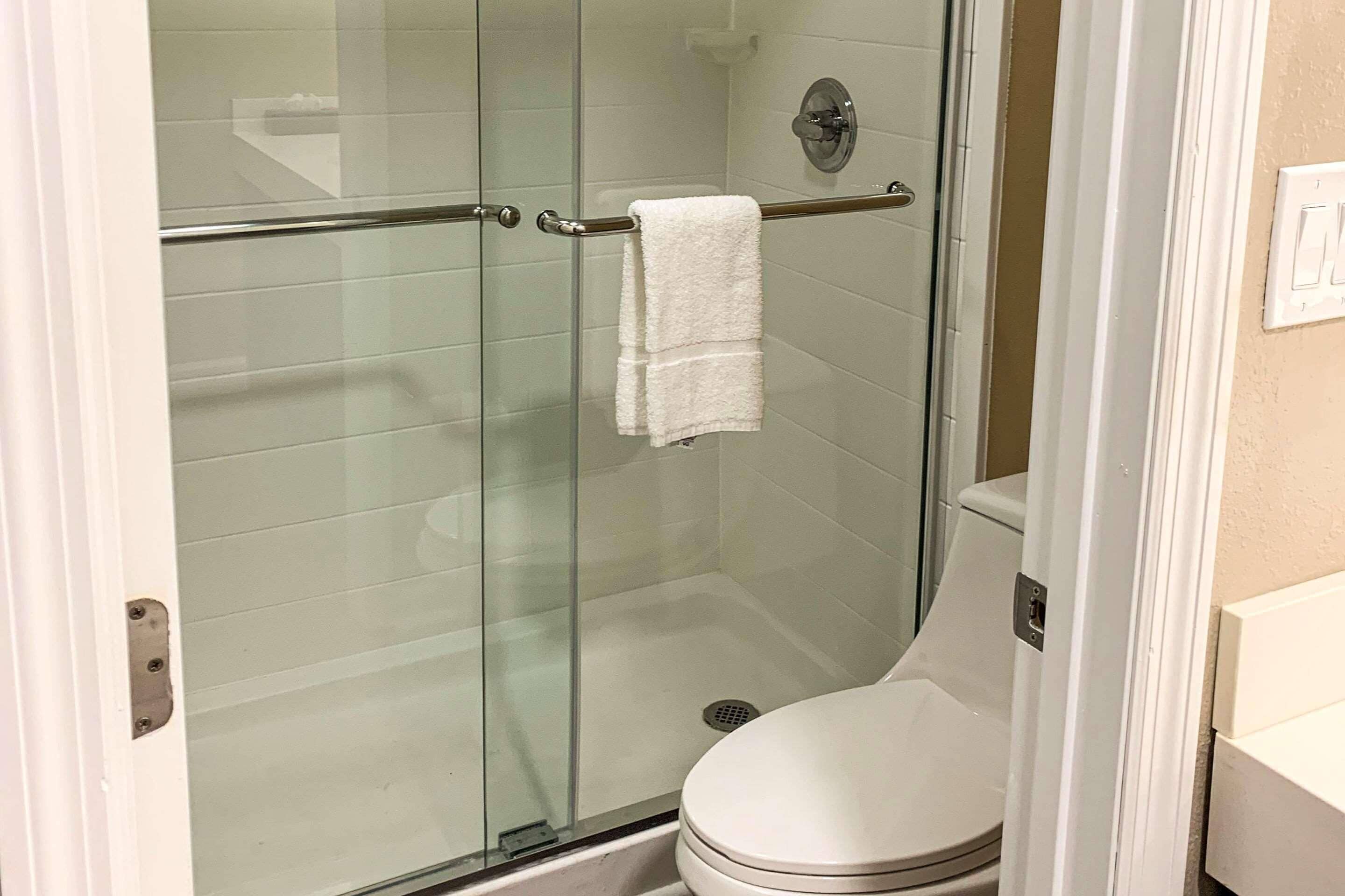 A glass-enclosed shower stall with a white towel hanging on a metal bar.