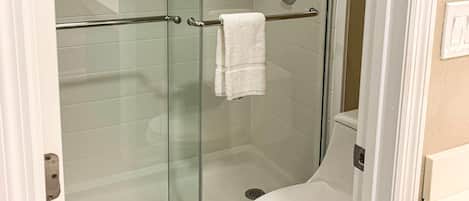 A glass-enclosed shower stall with a white towel hanging on a metal bar.