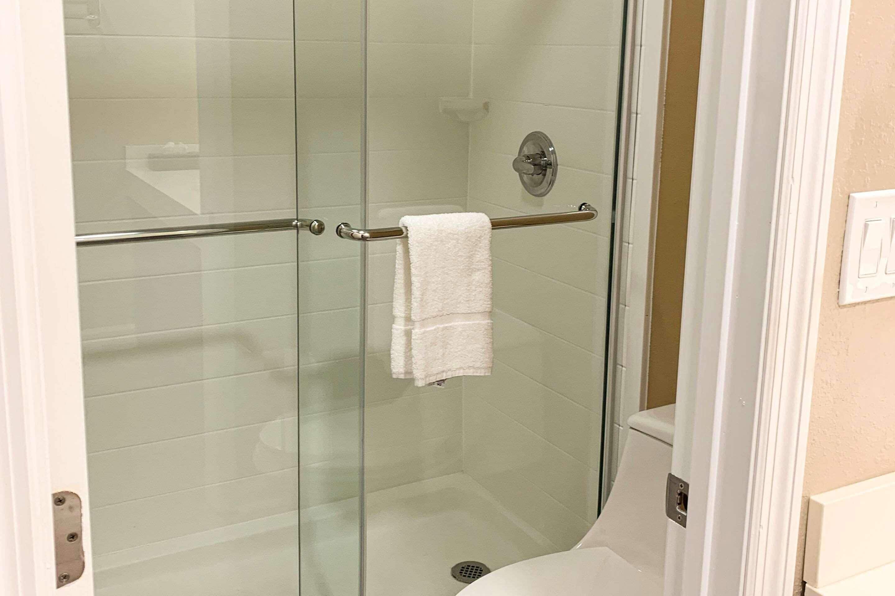 A glass-enclosed shower area with a white towel hanging on a metal bar.