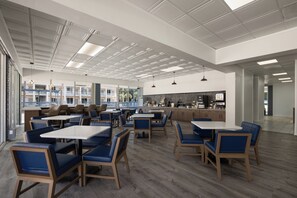 A spacious indoor dining area with multiple tables and chairs, a kitchen area, and a view of the outdoors.