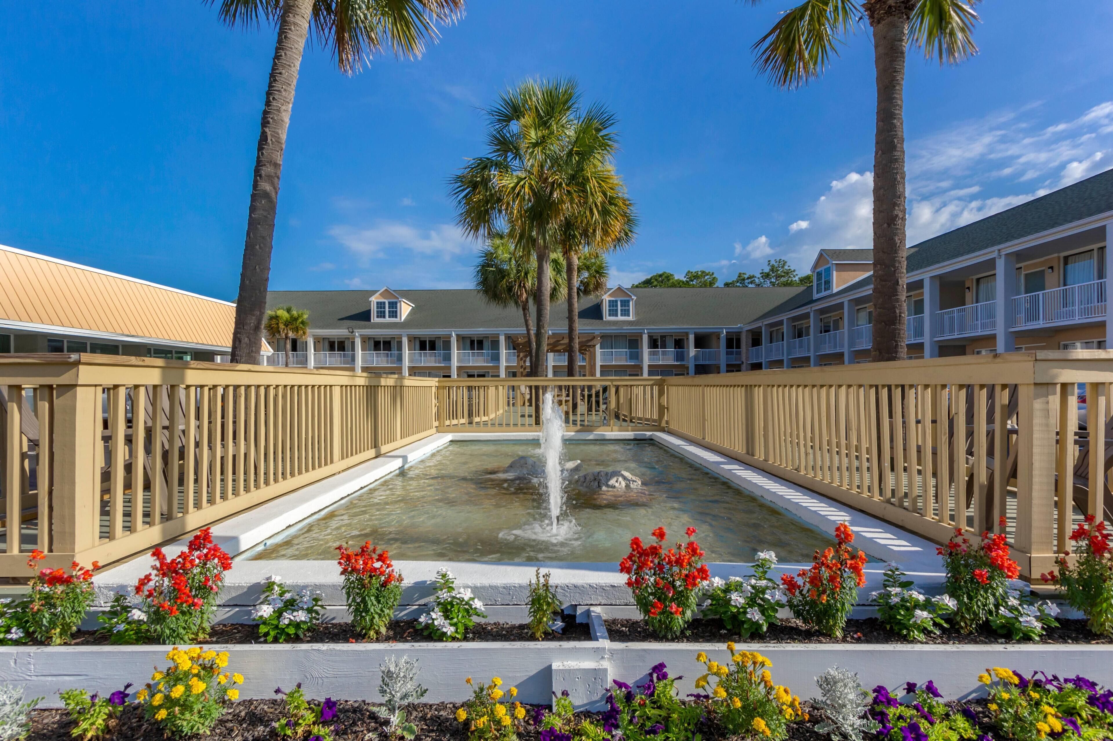 A hotel with a central courtyard featuring a fountain, surrounded by a wooden fence and various flower beds.