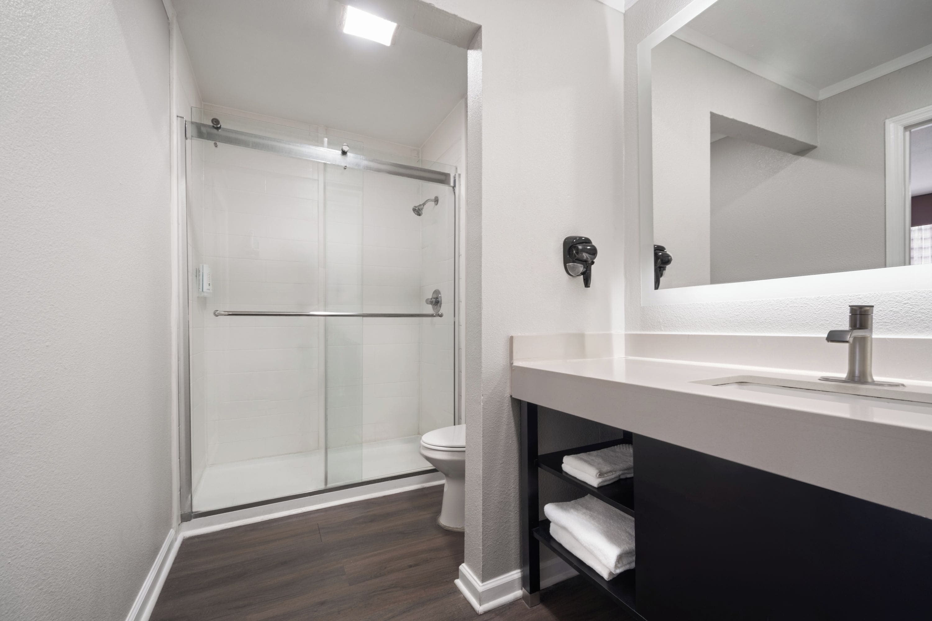 Un baño moderno con cabina de ducha de vidrio, inodoro blanco y tocador con espejo.