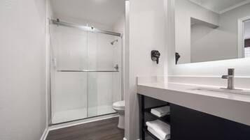 Un baño moderno con cabina de ducha de vidrio, inodoro blanco y tocador con espejo.