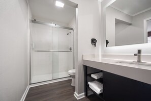 A modern bathroom with a glass shower enclosure, a white toilet, and a vanity with a mirror. - Baymont by Wyndham Pawleys Island (Pawleys Island)