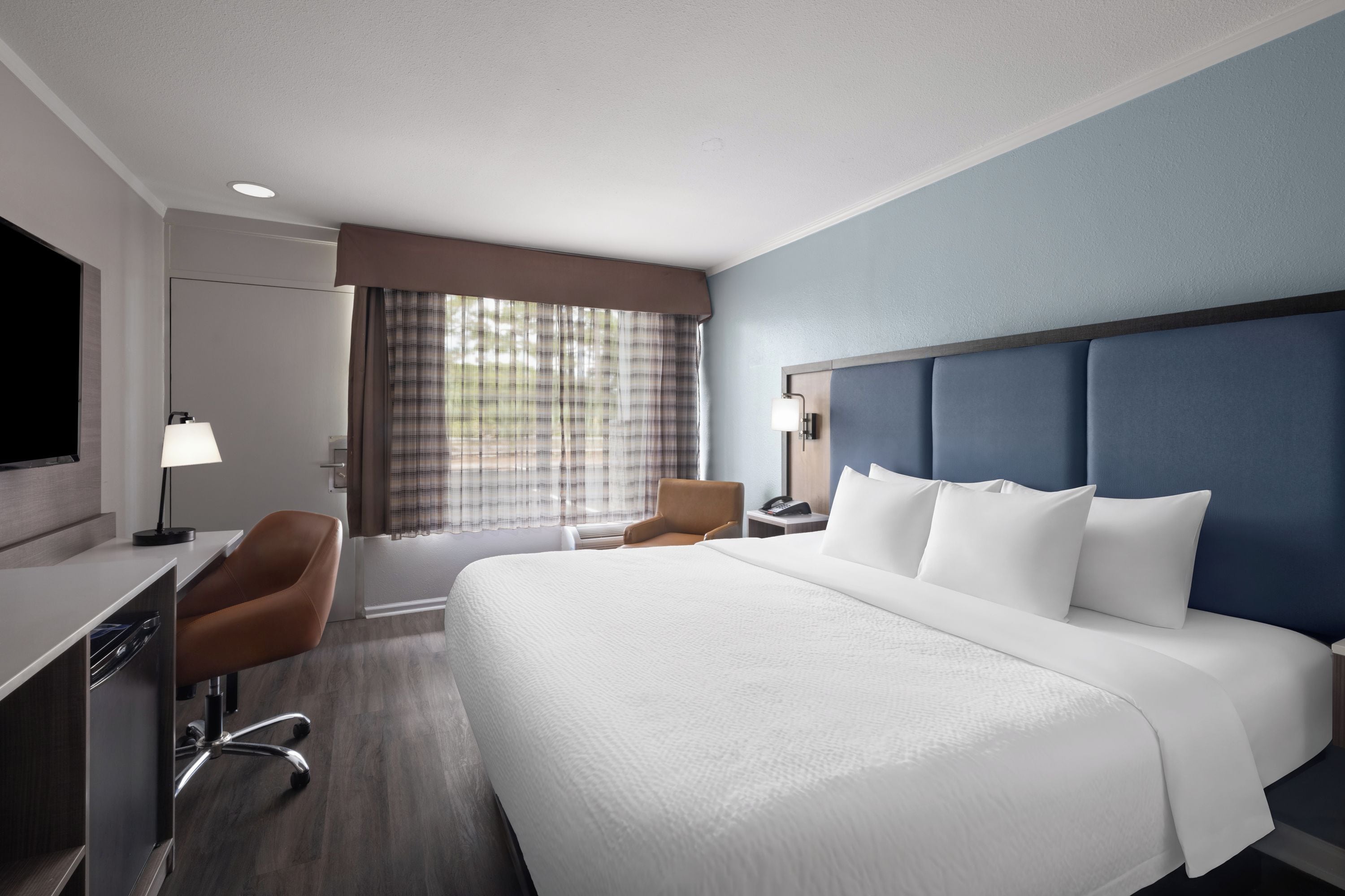 A hotel room with a large bed, a desk, a chair, a television, and a window with curtains.