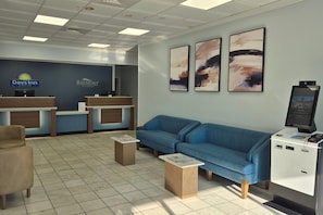 A hotel lobby with a reception desk, a blue sofa, a small coffee table, and artwork on the wall. - Baymont by Wyndham Pawleys Island (Pawleys Island)