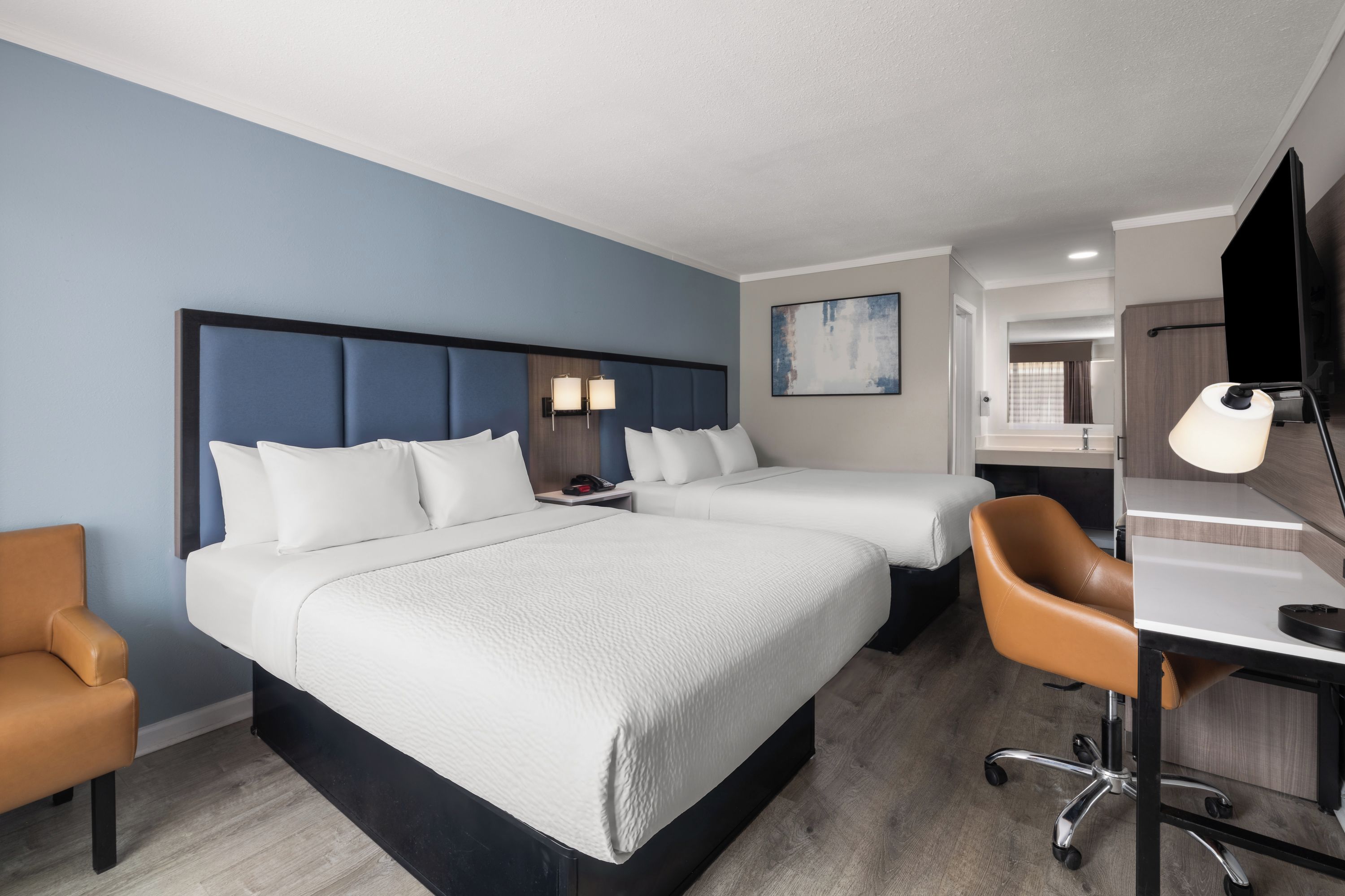 Una habitación de hotel con una cama grande, un escritorio, una silla y un baño visible a través de una puerta abierta.