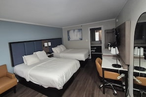 Habitación de hotel con dos camas, un escritorio, una silla, televisión y baño visible a través de una puerta abierta.