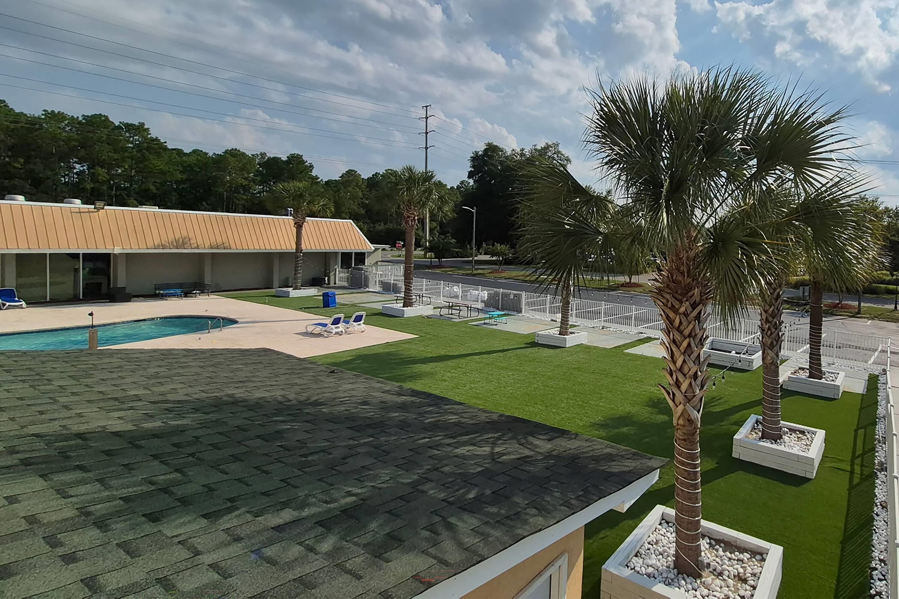 A swimming pool with lounge chairs, a building with a sloped roof, and palm trees.