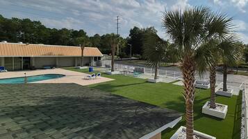 Uma piscina com espreguiçadeiras, um edifício com telhado inclinado e palmeiras.