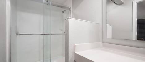 Een moderne badkamer met een glazen douchecabine, een wit toilet en een witte wastafel met een spiegel erboven.