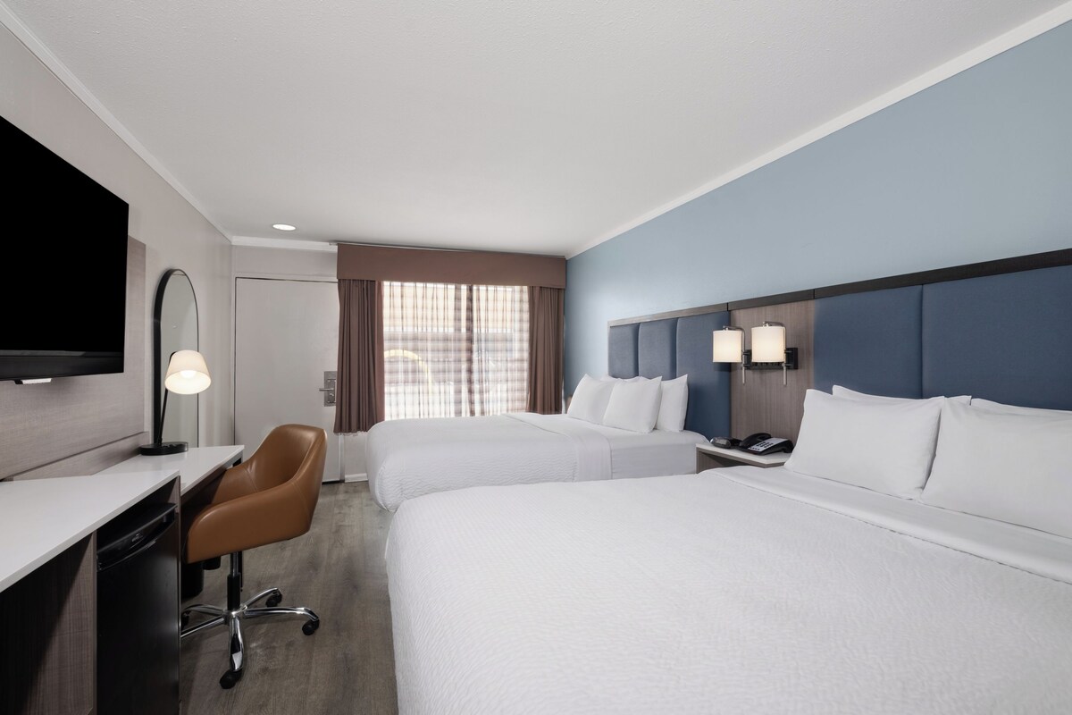 Habitación de hotel con dos camas, un escritorio, una silla, un televisor y una ventana con cortinas.