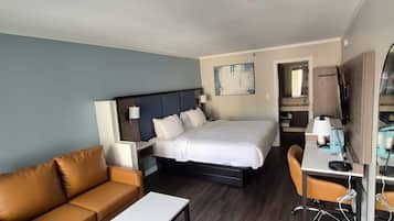 Habitación de hotel con cama, escritorio, silla, sofá y baño visible a través de una puerta abierta.