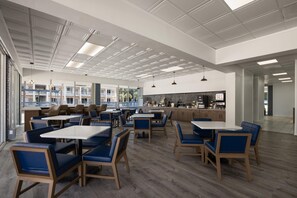 A spacious indoor area with multiple seating arrangements, a kitchen area, and a view of the outside. - Baymont by Wyndham Pawleys Island (Pawleys Island)