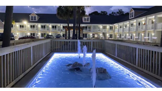 A hotel with a pool area featuring a water fountain, surrounded by a wooden deck and a fence. - Baymont by Wyndham Pawleys Island (Pawleys Island)