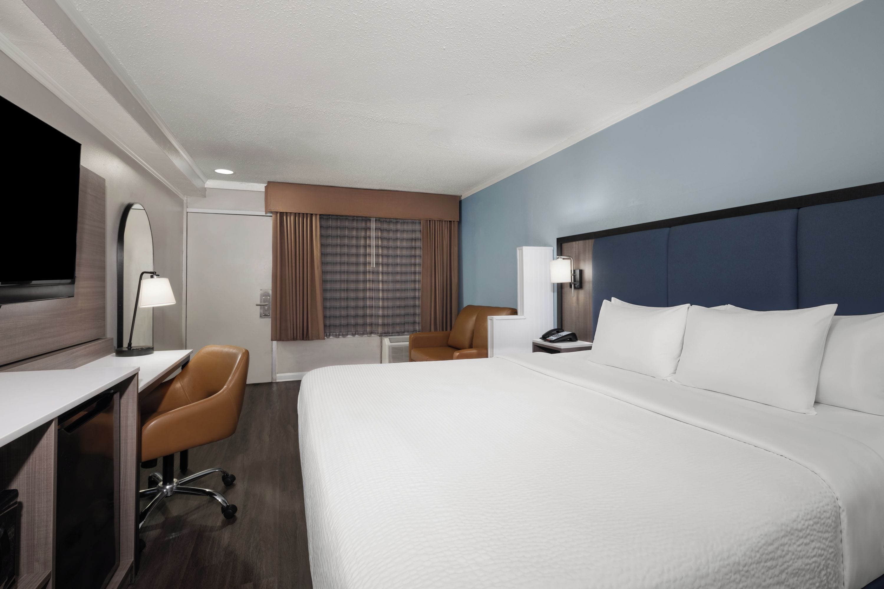 A hotel room with a bed, desk, chair, and a television.