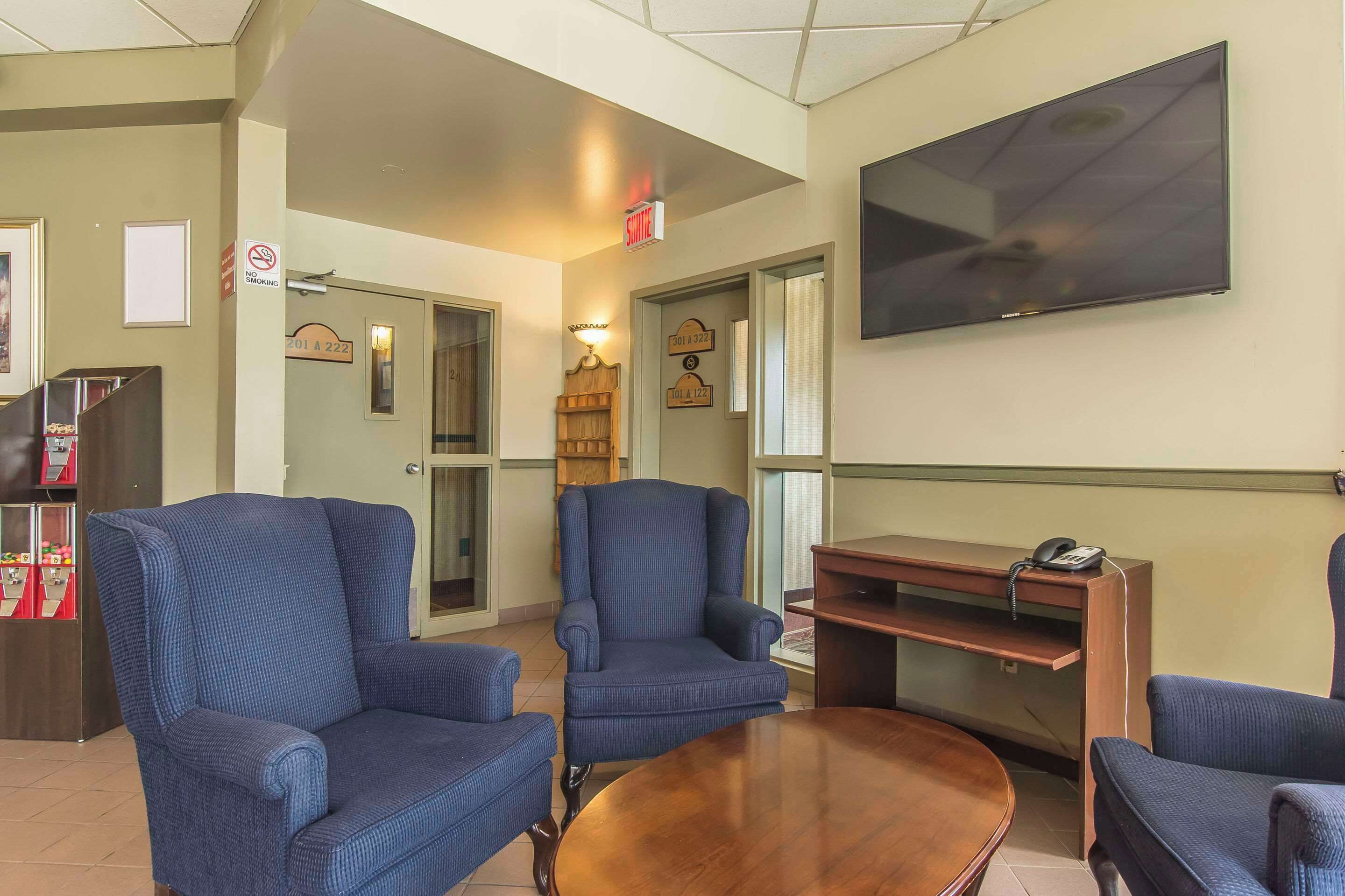 A lobby with blue armchairs, a wooden coffee table, a flat-screen TV, and a vending machine.