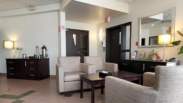 A hotel lobby with a reception desk, two armchairs, a small table, and a dark-colored counter. - Quality Hotel & Suites (Sherbrooke)