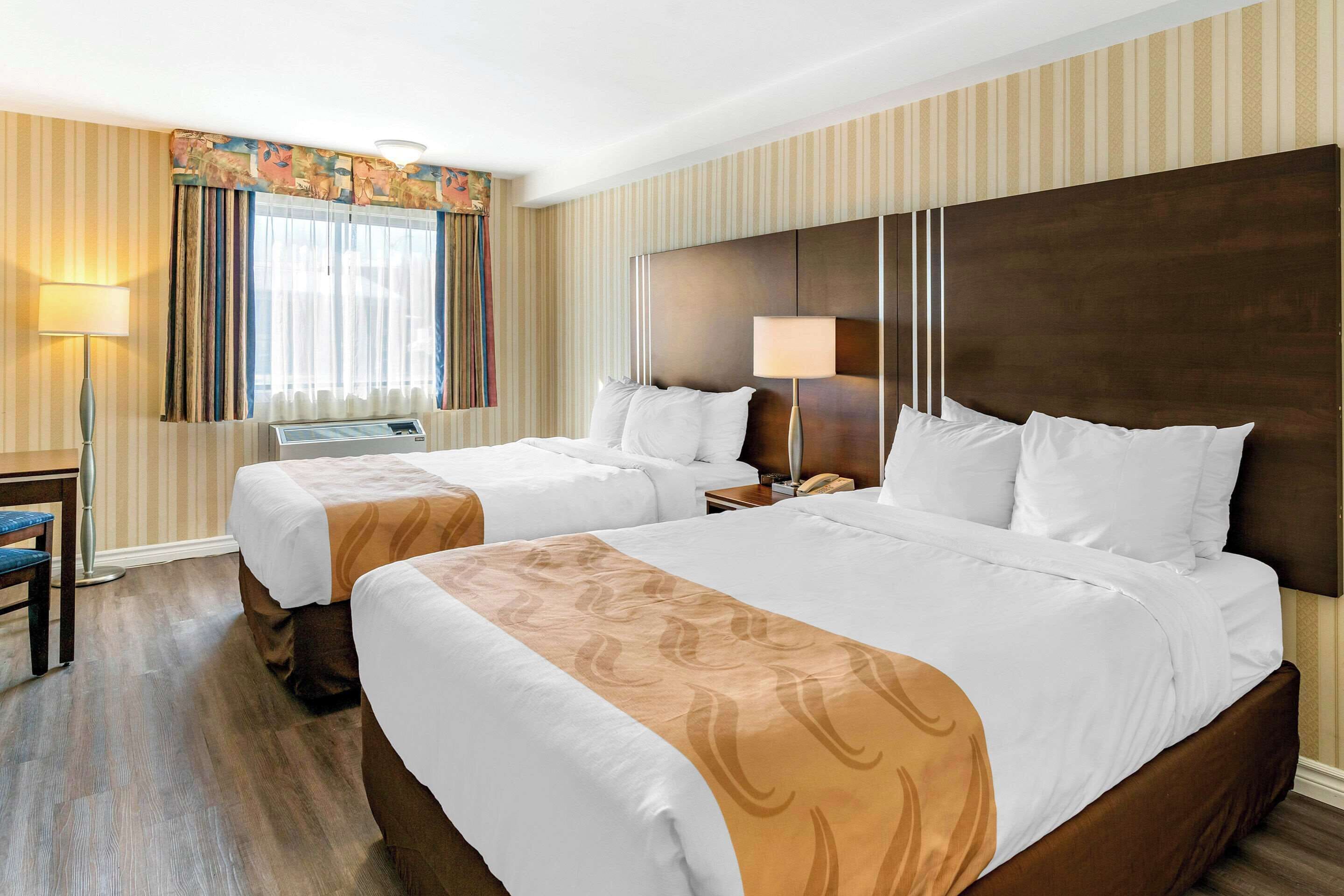 A hotel room with two beds, a desk, and a lamp.
