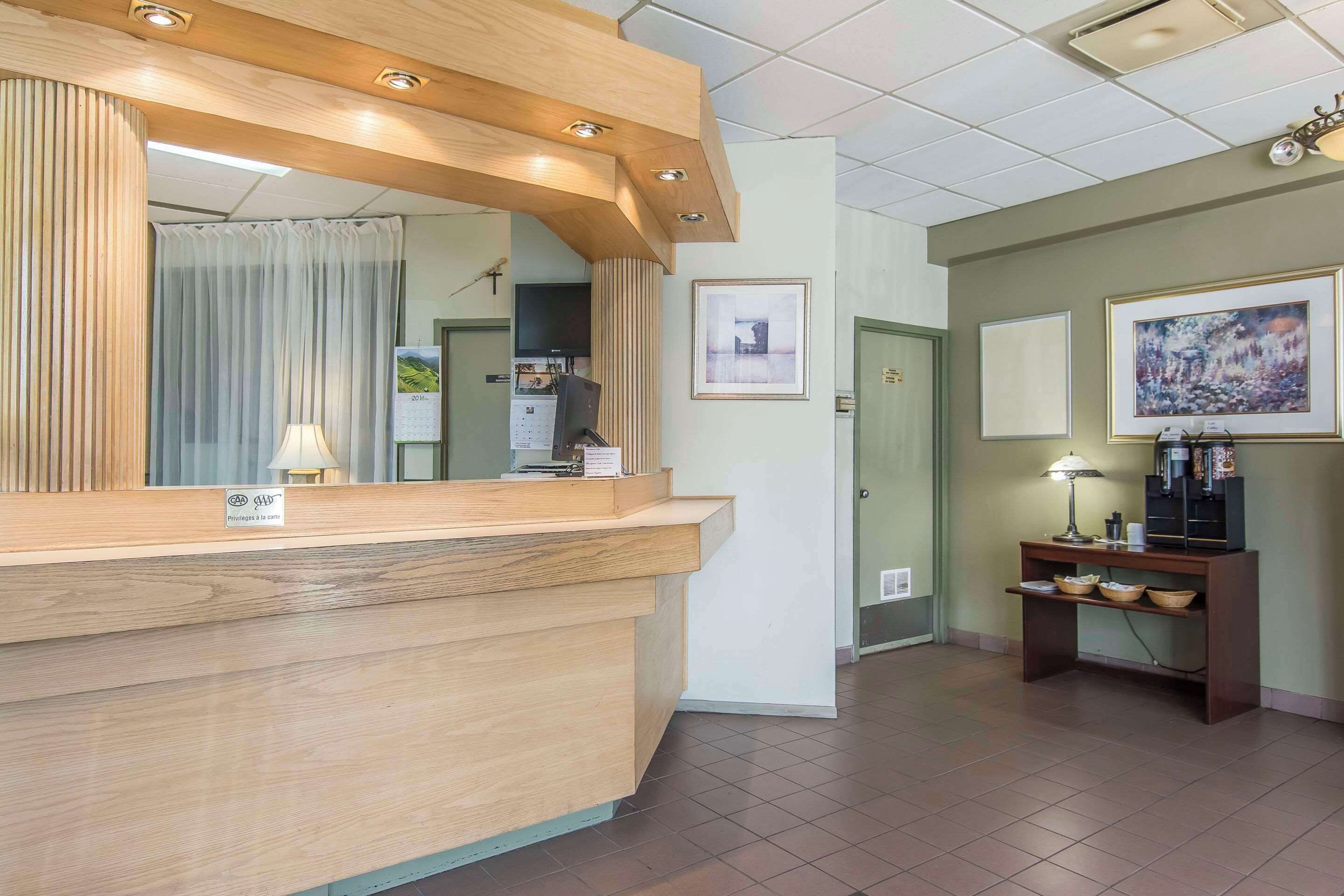 A reception area with a wooden counter, a mirror, a desk with a lamp, framed pictures on the wall, and a tiled floor.