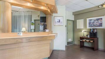 A reception area with a wooden counter, a mirror, a desk with a lamp, framed pictures on the wall, and a tiled floor.