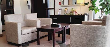 Un hall de hotel con dos sillones color beige, una mesa de madera oscura, un armario negro y un espejo grande sobre la mesa.