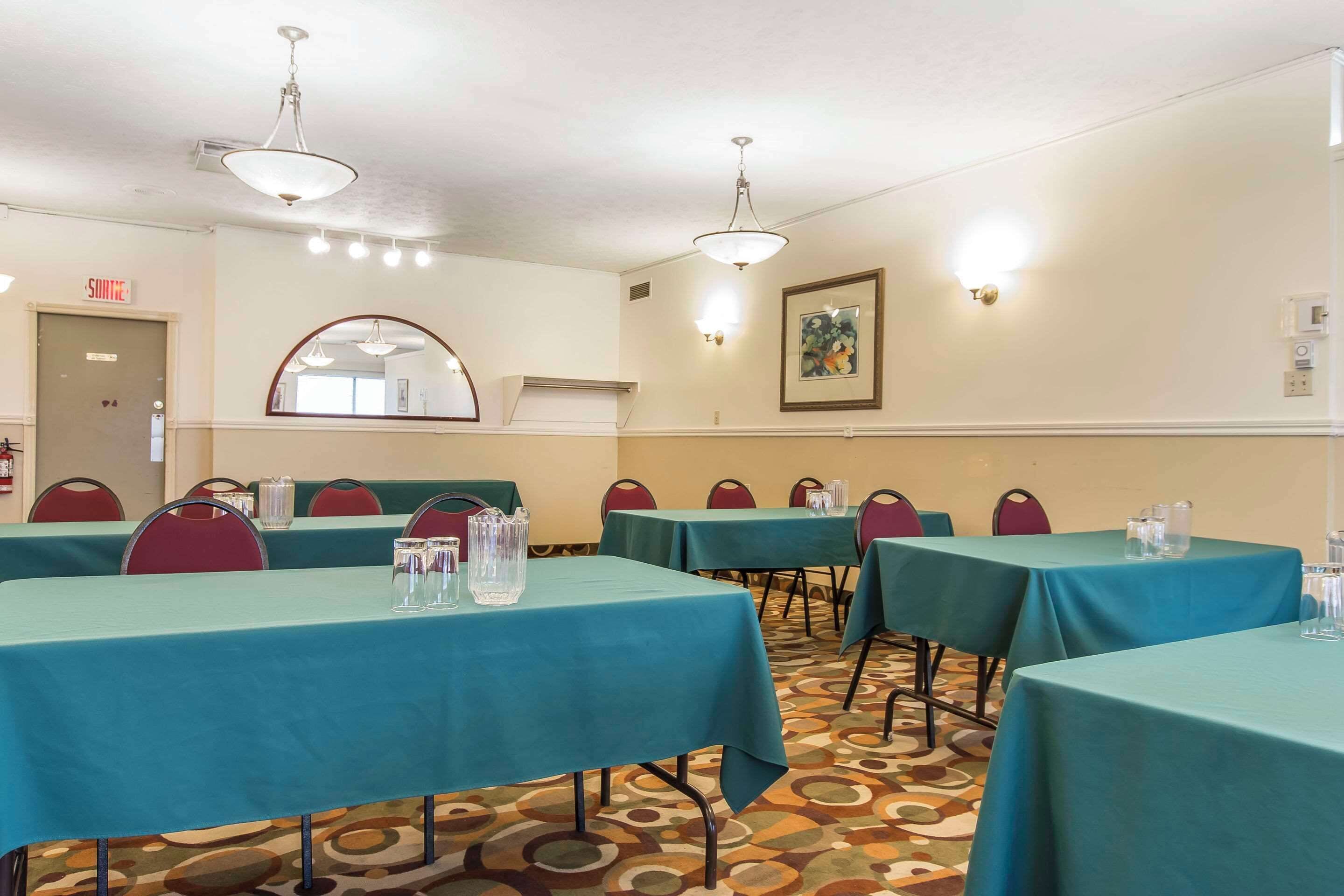 A conference room with teal tables and red chairs, equipped with water pitchers and glasses.