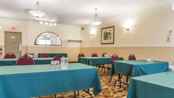 A conference room with teal tables and red chairs, equipped with water pitchers and glasses.