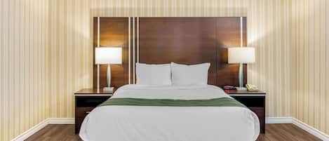 A hotel room with a large bed, two bedside tables with lamps, and striped wallpaper.