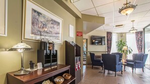 A lobby with a reception desk, framed artwork, a television, seating area, and a plant. - Quality Hotel & Suites (Sherbrooke)