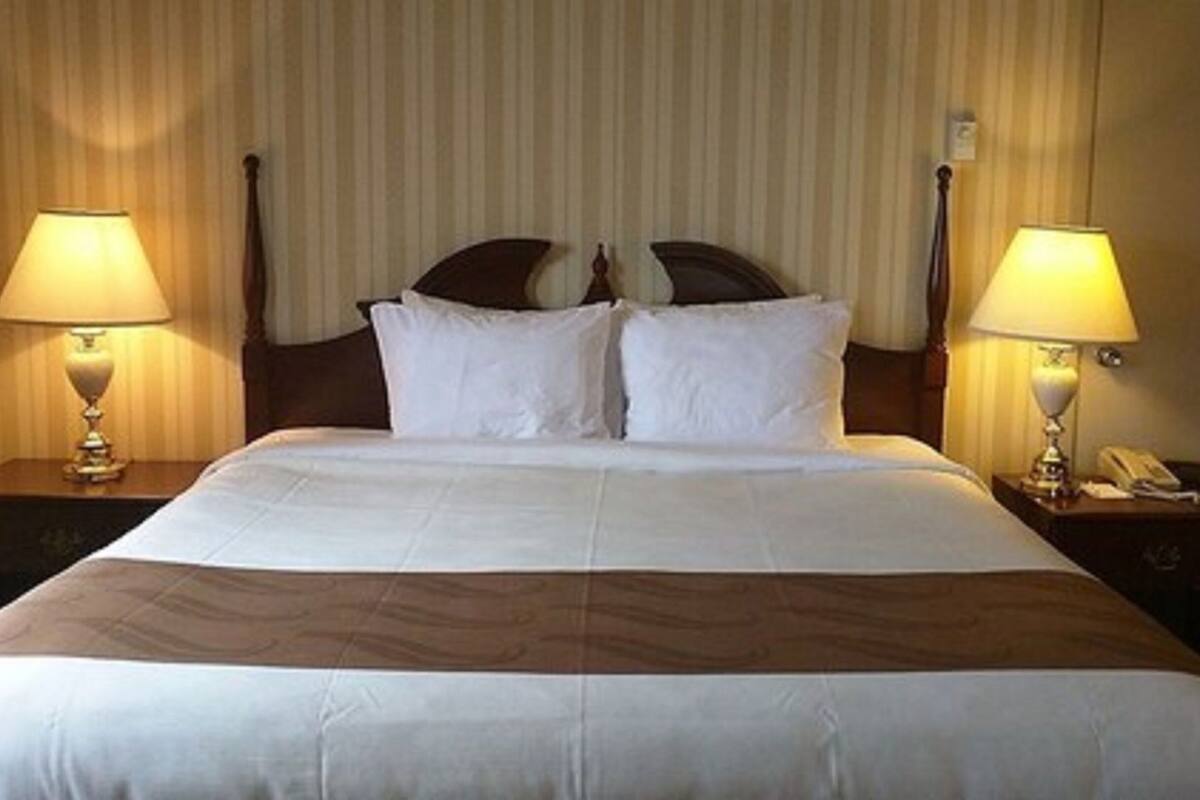 Habitación de hotel con una cama grande, dos lámparas de noche, un teléfono y una cortina.