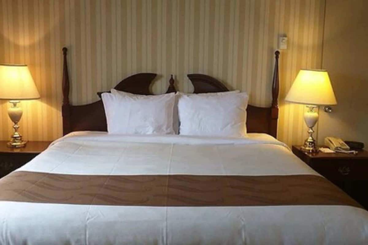 Una habitación de hotel con una cama grande, dos mesitas de noche con lámparas y un teléfono en una de ellas.