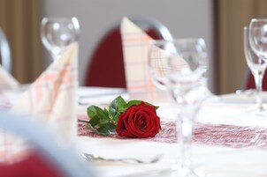 Una mesa de comedor con una rosa roja, copas de cristal transparentes y una servilleta escocesa.