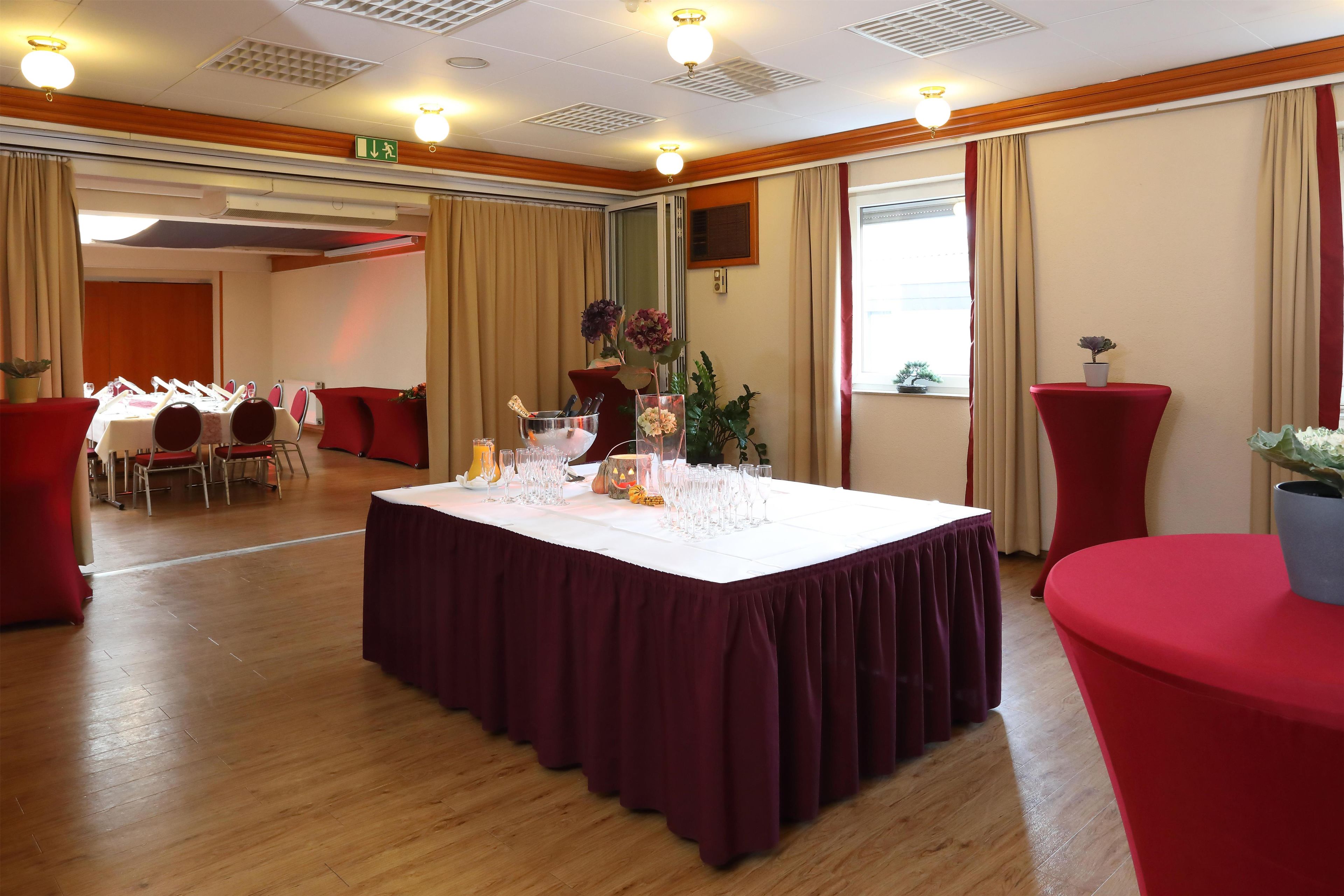 Un salón de conferencias con una larga mesa dispuesta para una reunión, equipado con sillas, un atril y una pantalla grande.