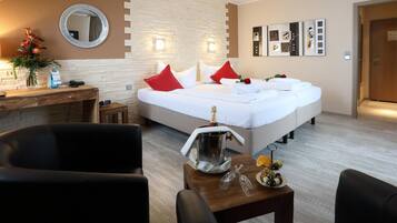 A hotel room with a large bed, a desk with a telephone, a mirror, and a wall with framed pictures.