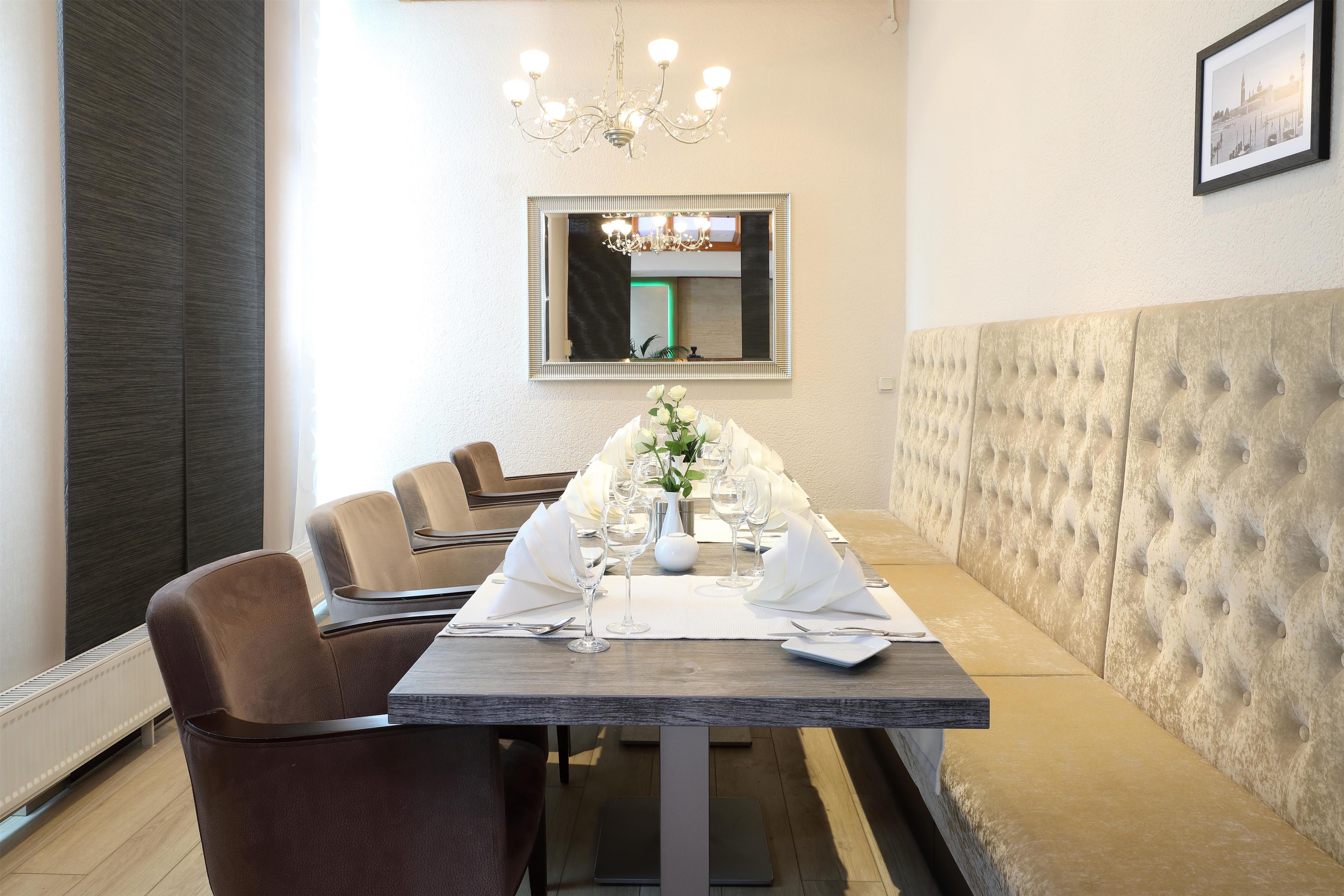 Un comedor con una mesa larga dispuesta para una comida, sillas, una araña y un espejo en la pared.