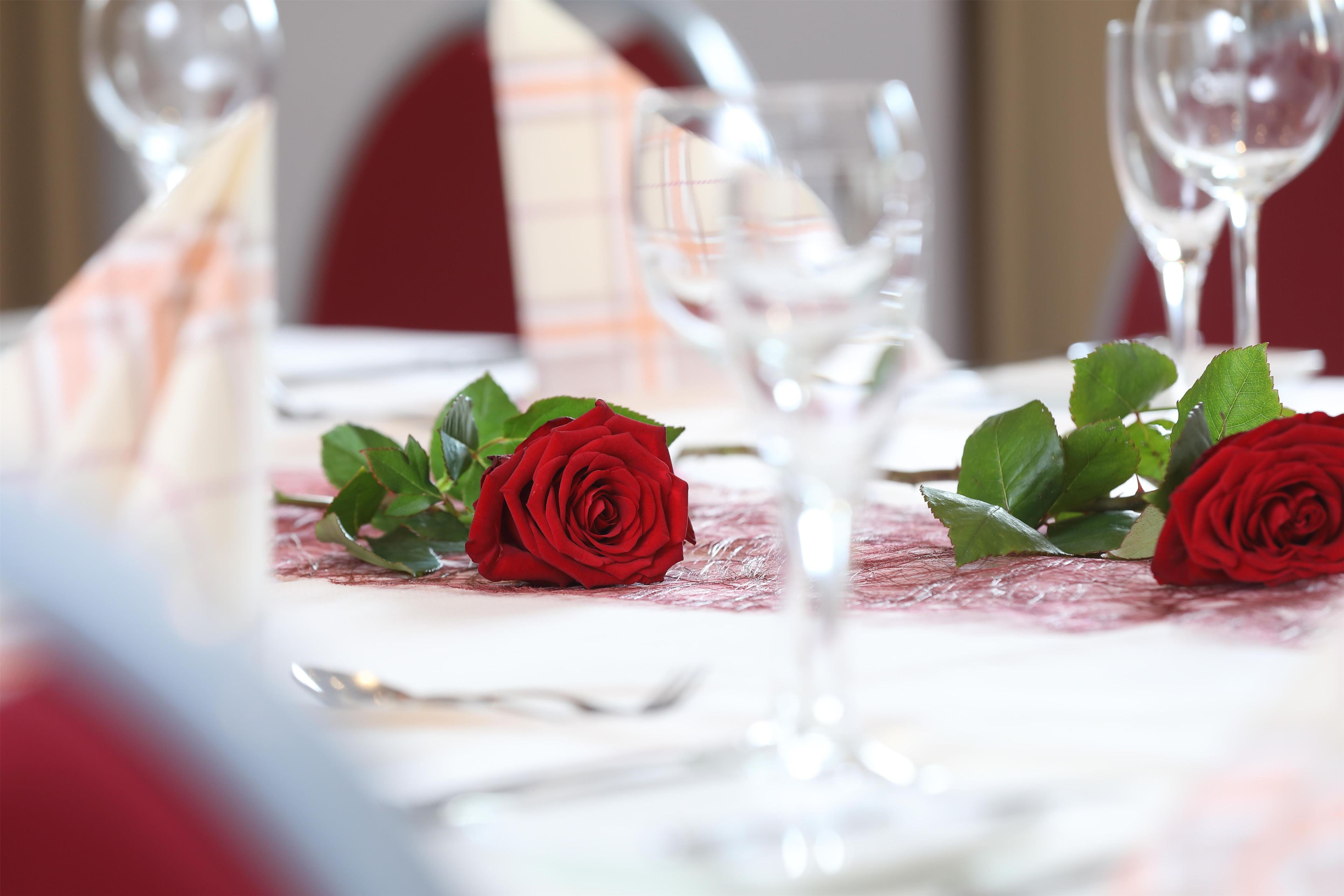 A table set for dining with wine glasses and red roses.