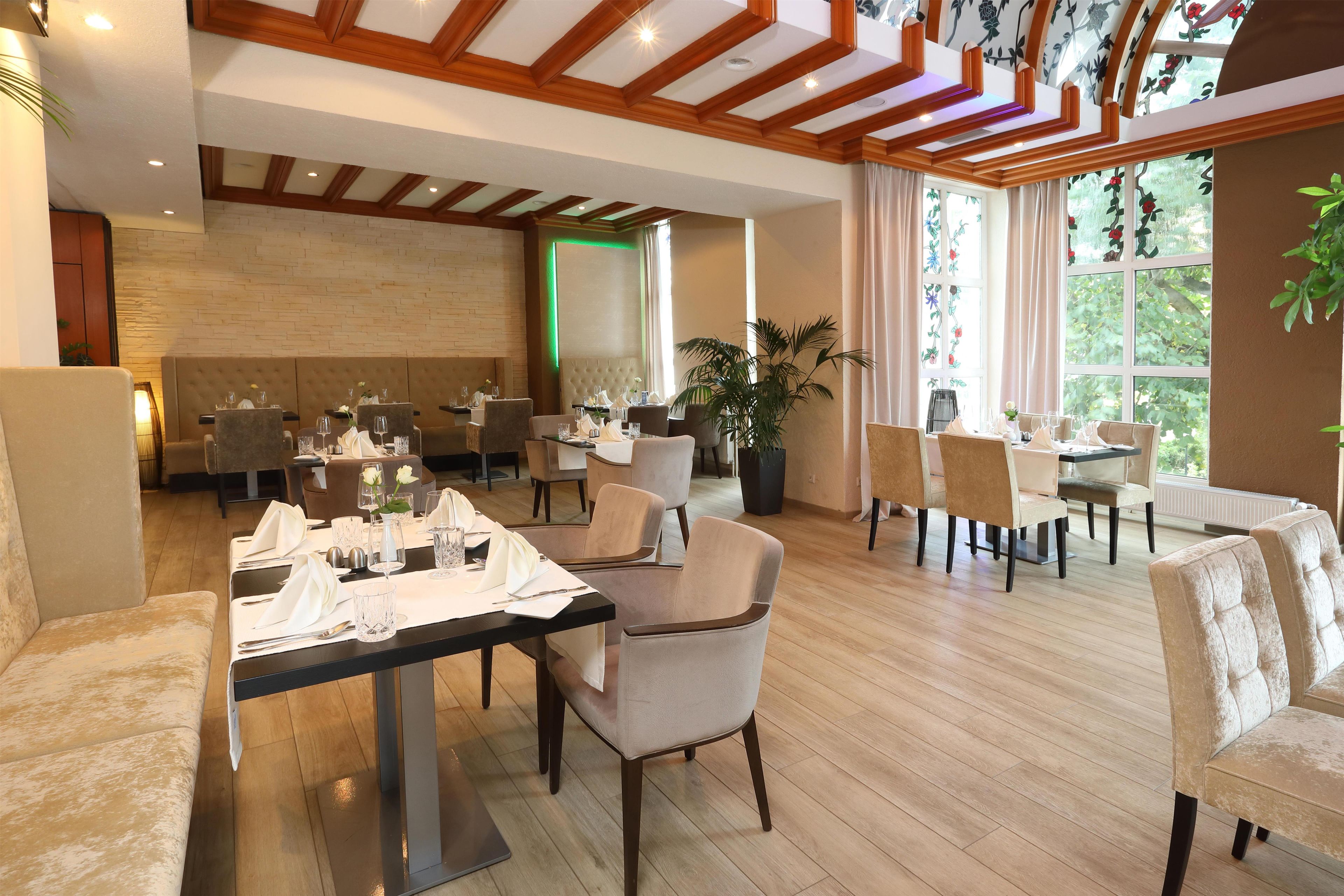 Un restaurant doté de plusieurs tables, de chaises et d’une grande fenêtre offrant une vue sur la verdure.