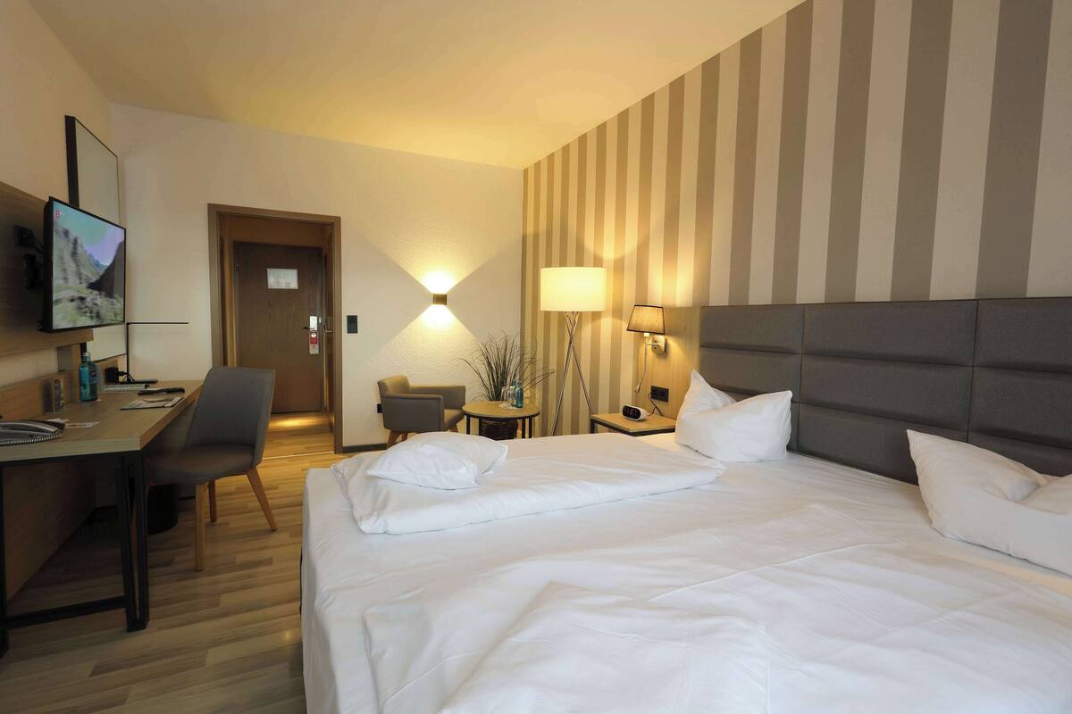 A hotel room with a bed, a desk, a chair, a TV, and a lamp.