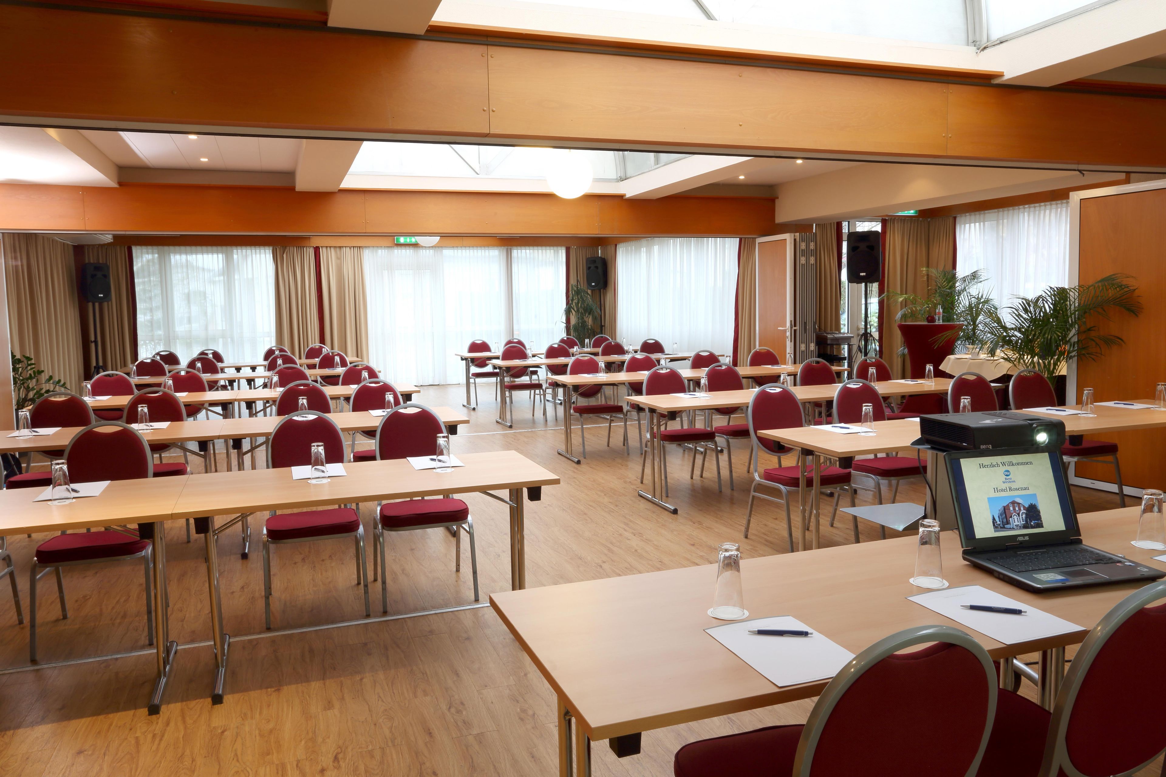 Un salón de conferencias con varias mesas y sillas, equipado con computadoras portátiles, vasos de agua y documentos.