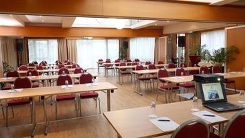 Un salón de conferencias con varias mesas y sillas, equipado con computadoras portátiles, vasos de agua y documentos.