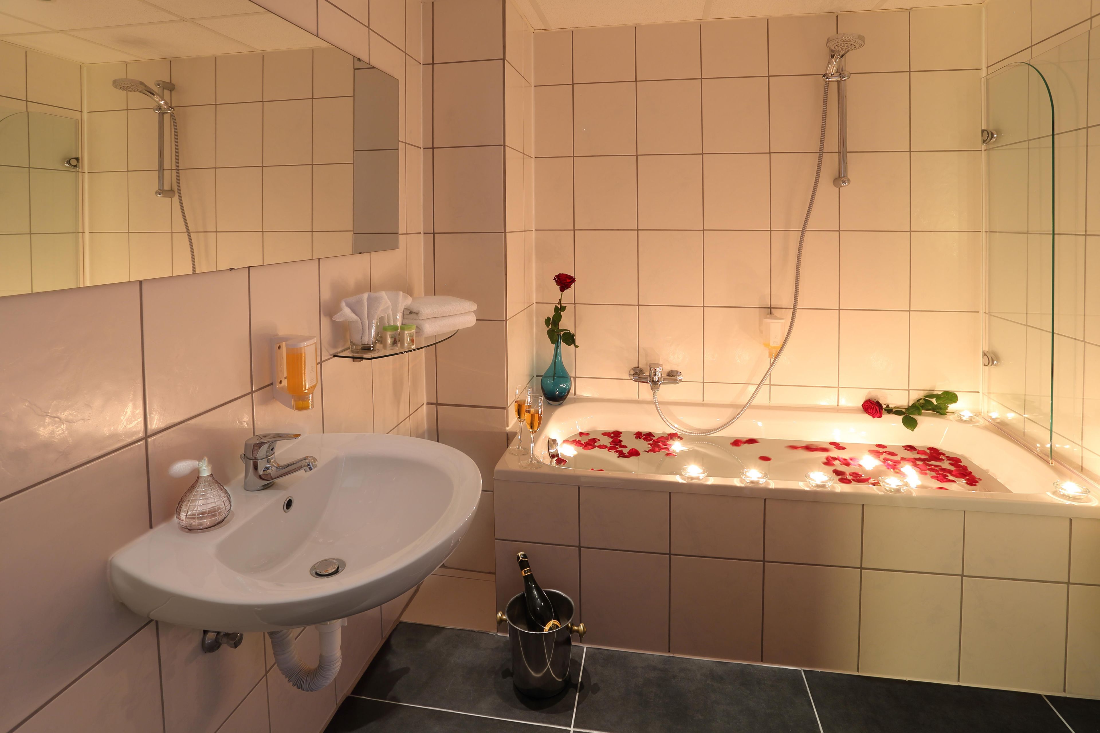 Ein Badezimmer mit einem weißen Waschbecken, einer Badewanne mit Rosenblüten und Kerzen sowie einer Dusche.